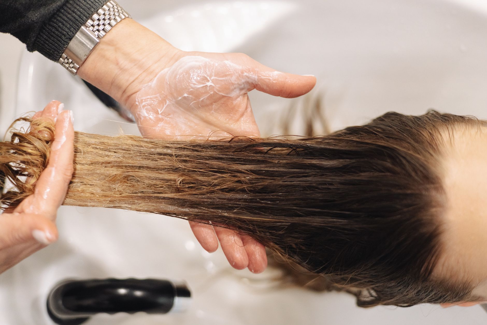Manos que reparten un producto capilar sobre el pelo húmedo en un lavacabezas