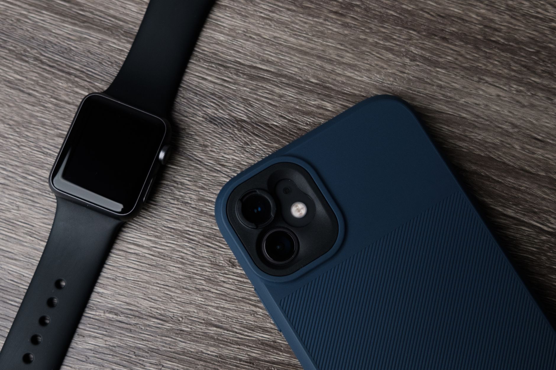 Reloj de correa negra junto a un móvil con funda azul sobre madera