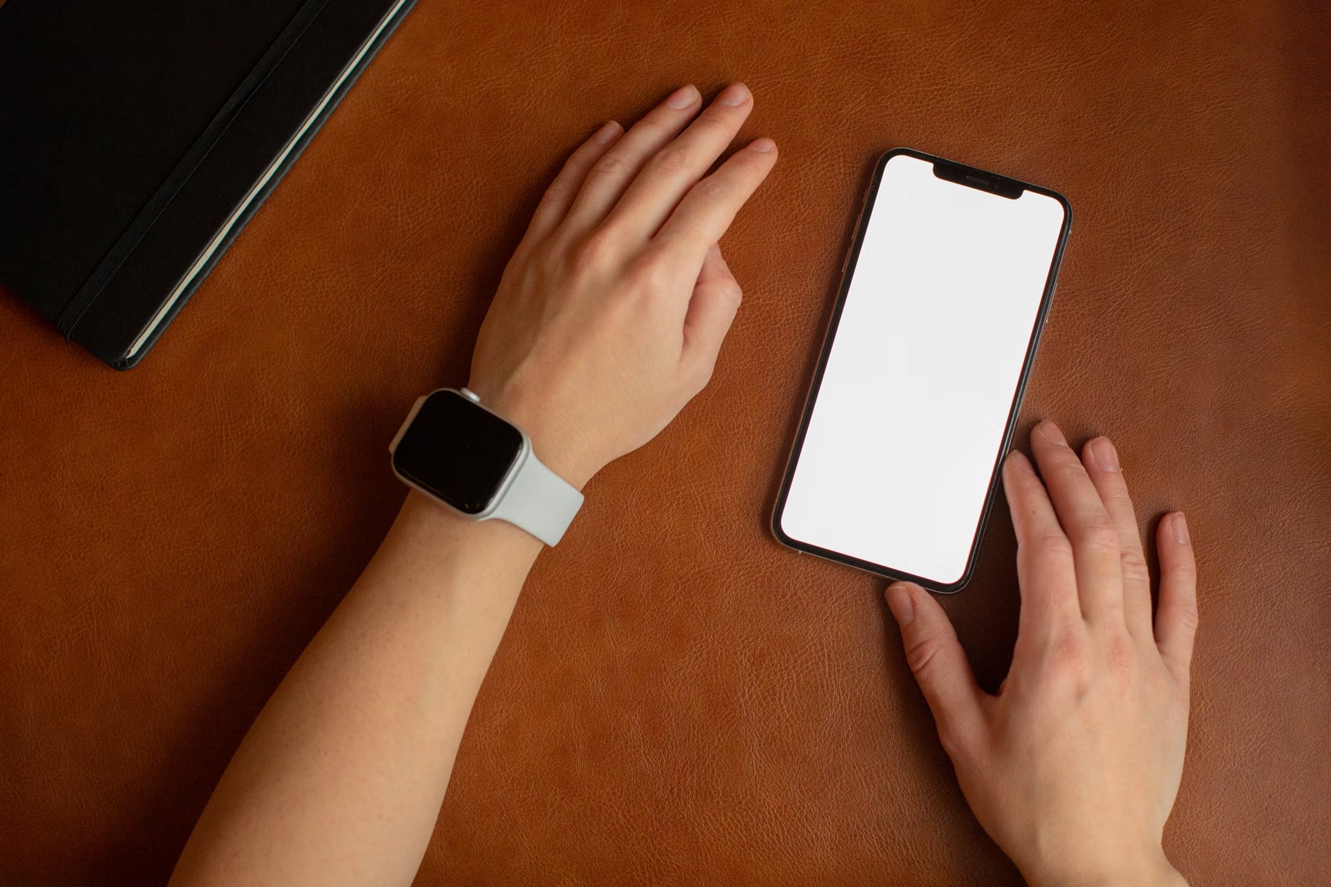 Una persona con un reloj de correa clara junto a un móvil de pantalla blanca